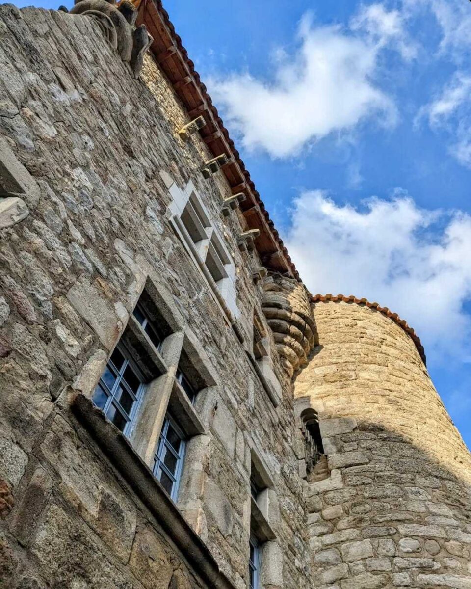 Photo du château du Bruget à Jaujacen zoom sur les fenêtres, avec les détails architecturaux et une des tours sur fond de ciel bleu avec de jolies nuages blancs