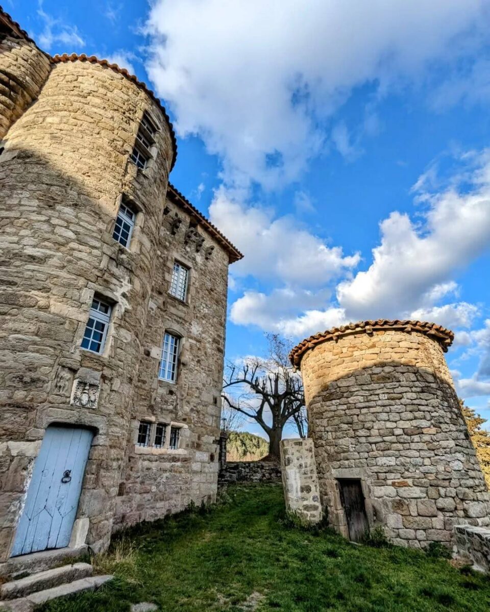 Photo du château du Bruget à Jaujac sur son flanc sud avec la tour de l'escalier sur fond de ciel bleu avec de jolies nuages blancs