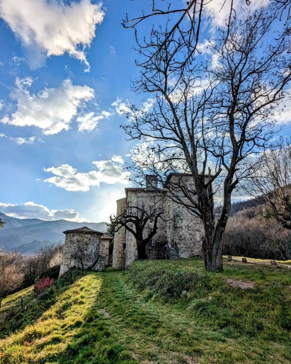Photo du château du Bruget à Jaujac sur ciel bleu avec de jolies nuages blancs et en fond le massif du Tanargue en Ardèche