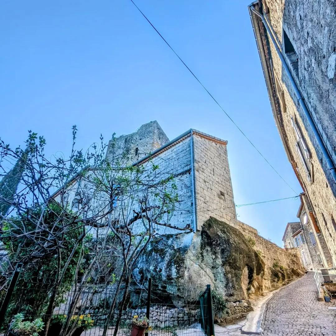 Vue sur les remparts et le donjon du château de Montréal en Ardèche depuis la rue pavé qui monte vers le haut du village (photo)
